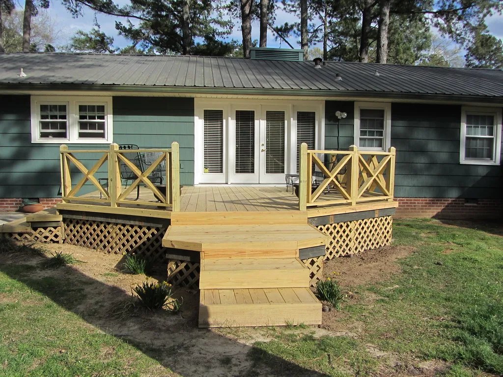 New wood deck with wide steps and railings behind the same house