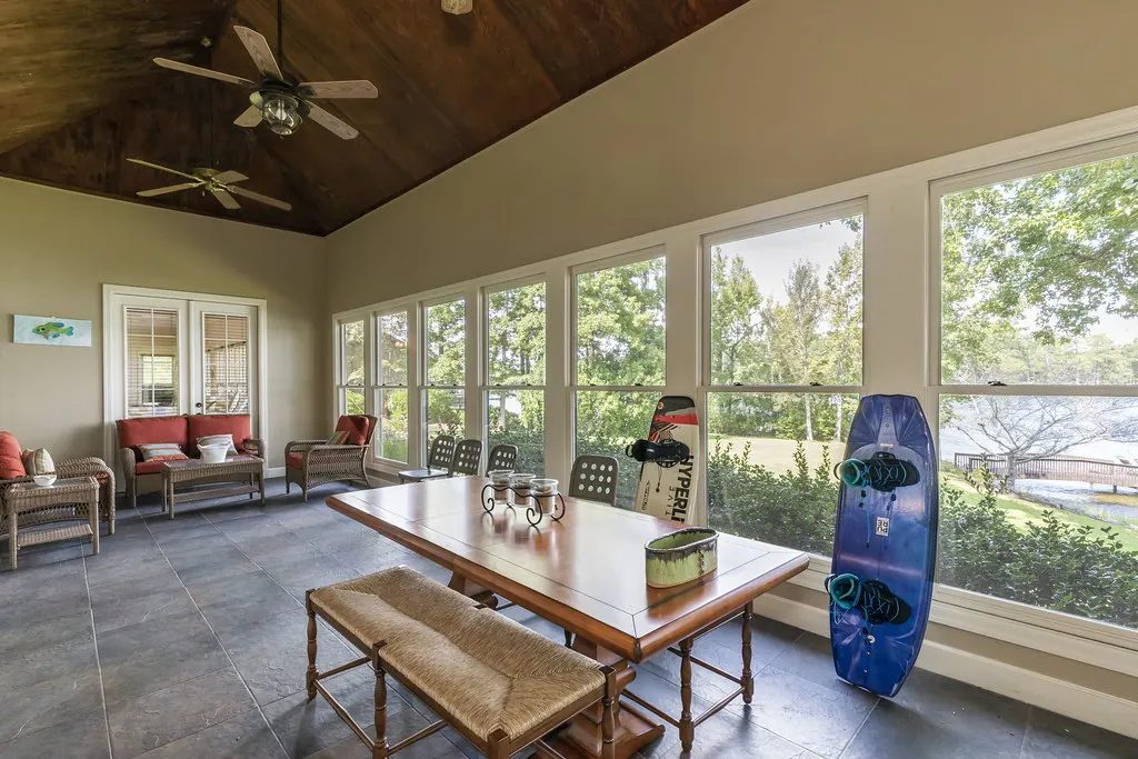 Bright sunroom interior with windows on three sides, ceiling fans and a long table